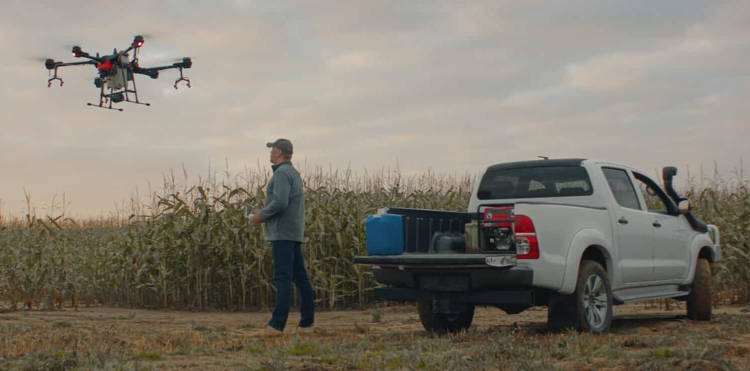 Farmer using a tablet to control and monitor a drone in a crop field, displaying live agricultural analytics on screen.